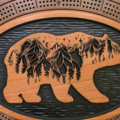 Walnut bear cribbage board beside a rustic mountain landscape plaque